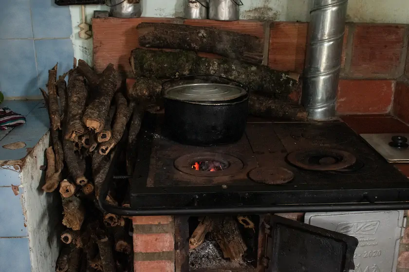 Con el calor de la estufa, uno de los beneficiarios seca los maderos fragmentados de un tronco de naranjo que se desplomó en su predio, ubicado en la cabecera del corregimiento San Vicente. Fotografía: Angie Serna Morales.